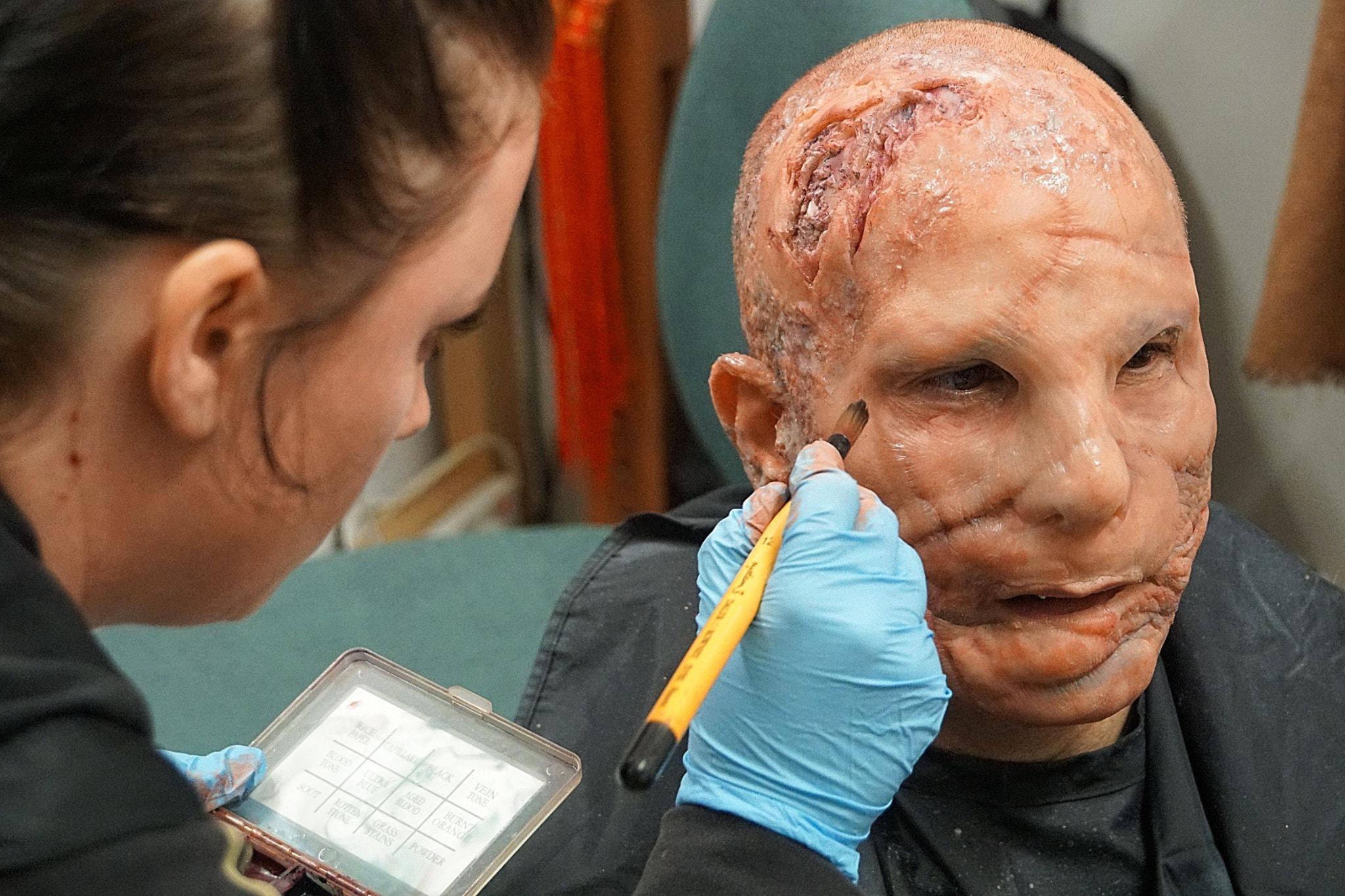 A makeup artist finishing extensive burn-effect prosthetics on Peter Pedrero — Dredd — Concept film